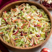 Homemade apple slaw with shredded cabbage, apples, carrots, almonds and dressing shown in a wooden salad bowl.