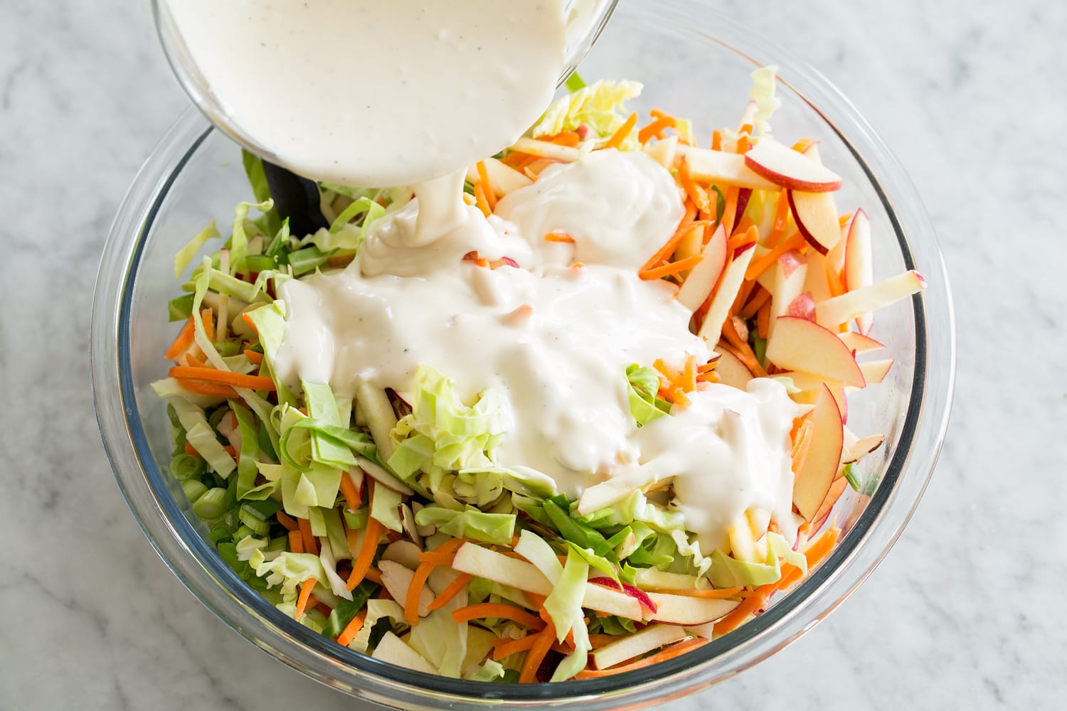 Slaw being topped with dressing.