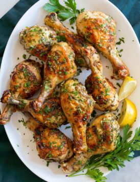 Baked chicken legs on a white oval platter with parsley and lemon wedges to the side.