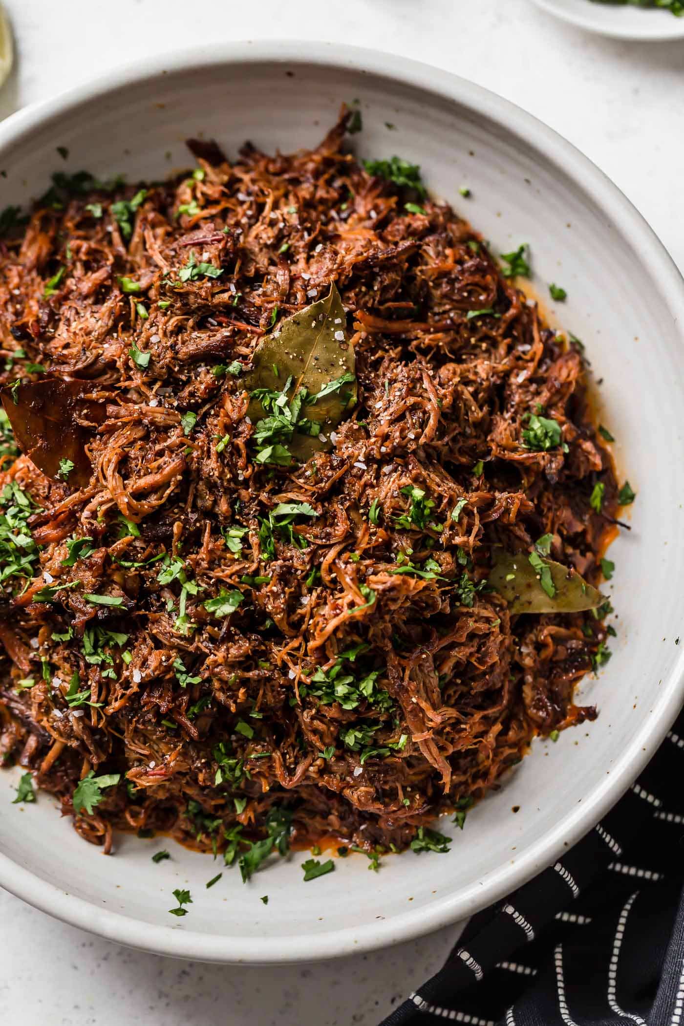 Slow cooker shredded barbacoa beef in a white serving bowl garnished with cilantro.
