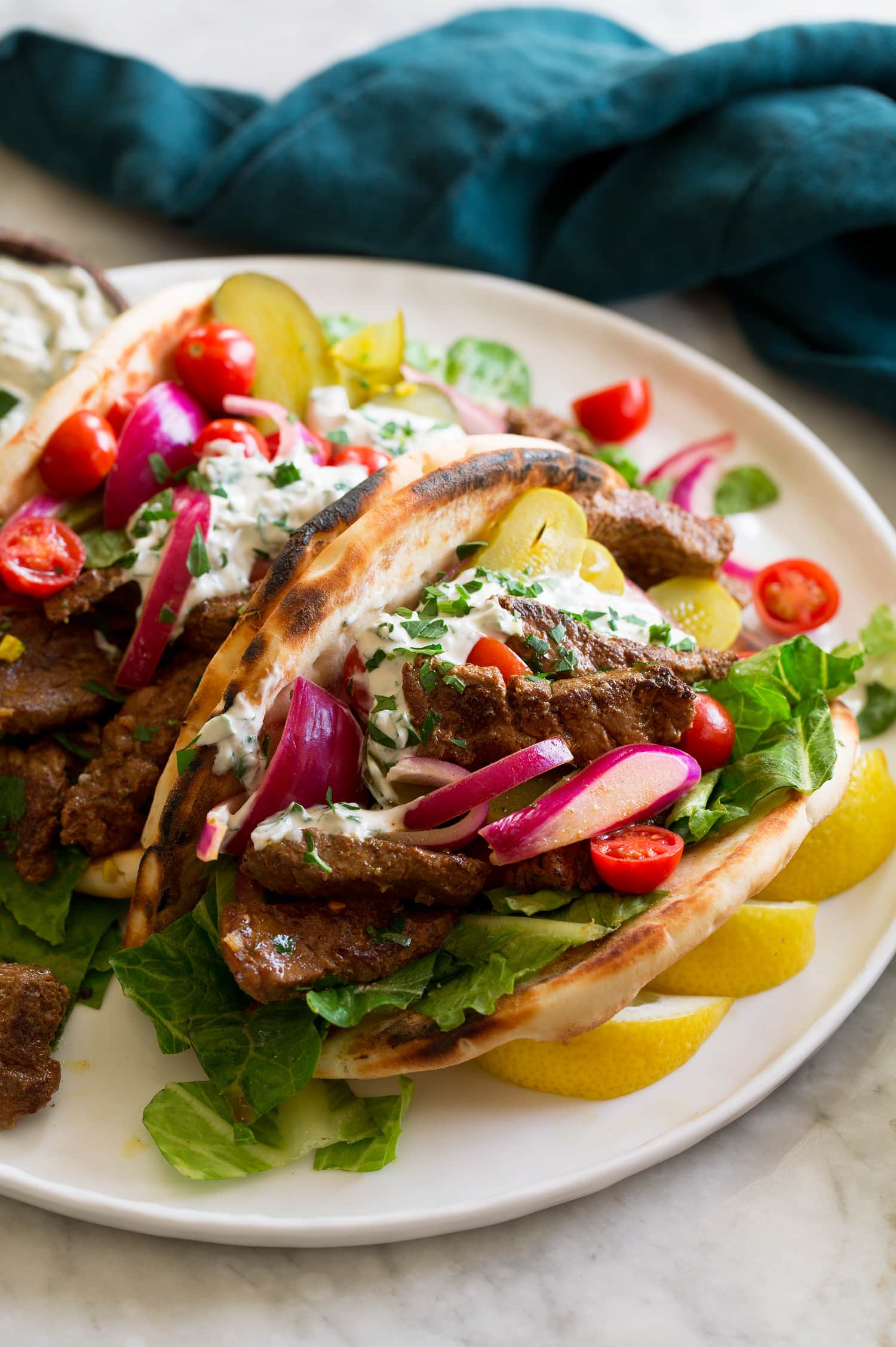 Beef shawarma shown in a pita with lettuce, tomatoes, red onion, pickles and a tahini yogurt sauce.