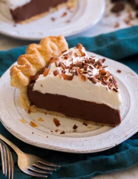 Close up photo of single slice chocolate cream pie that's made with a homemade pie crust, topped with whipped cream and finished with chocolate curls.