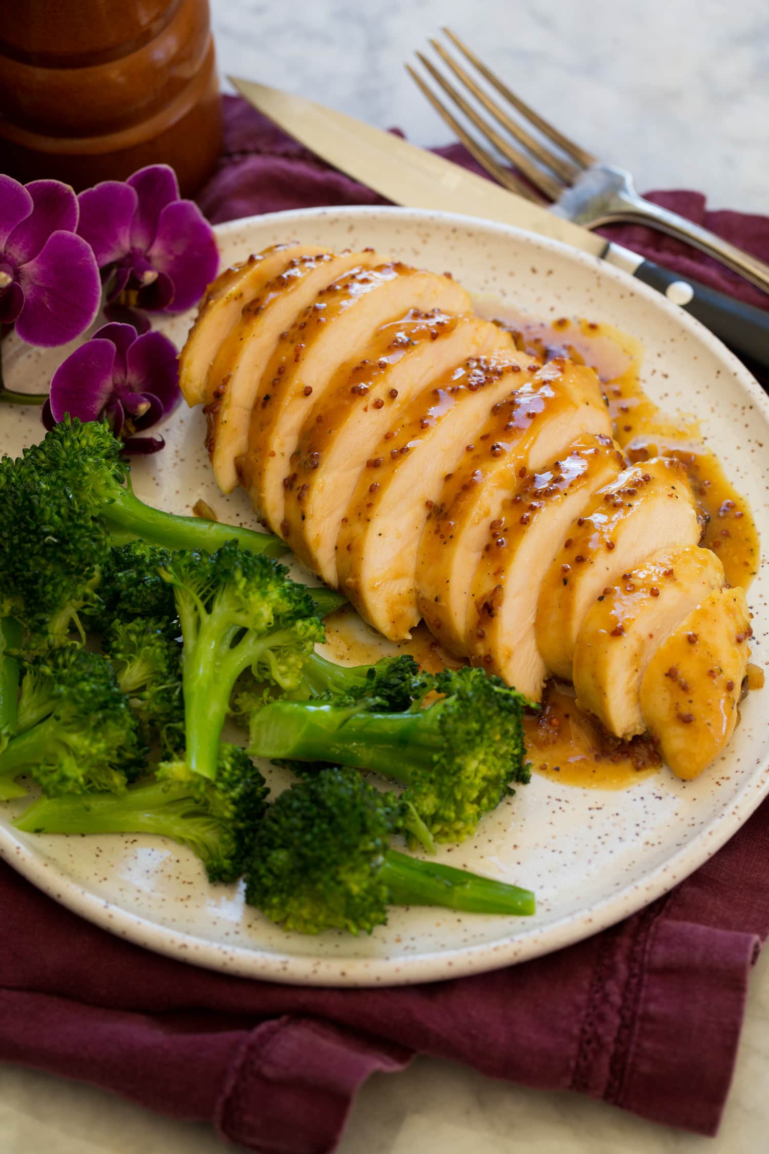 Sliced chicken with honey mustard on a plate with steamed broccoli as a serving suggestion.