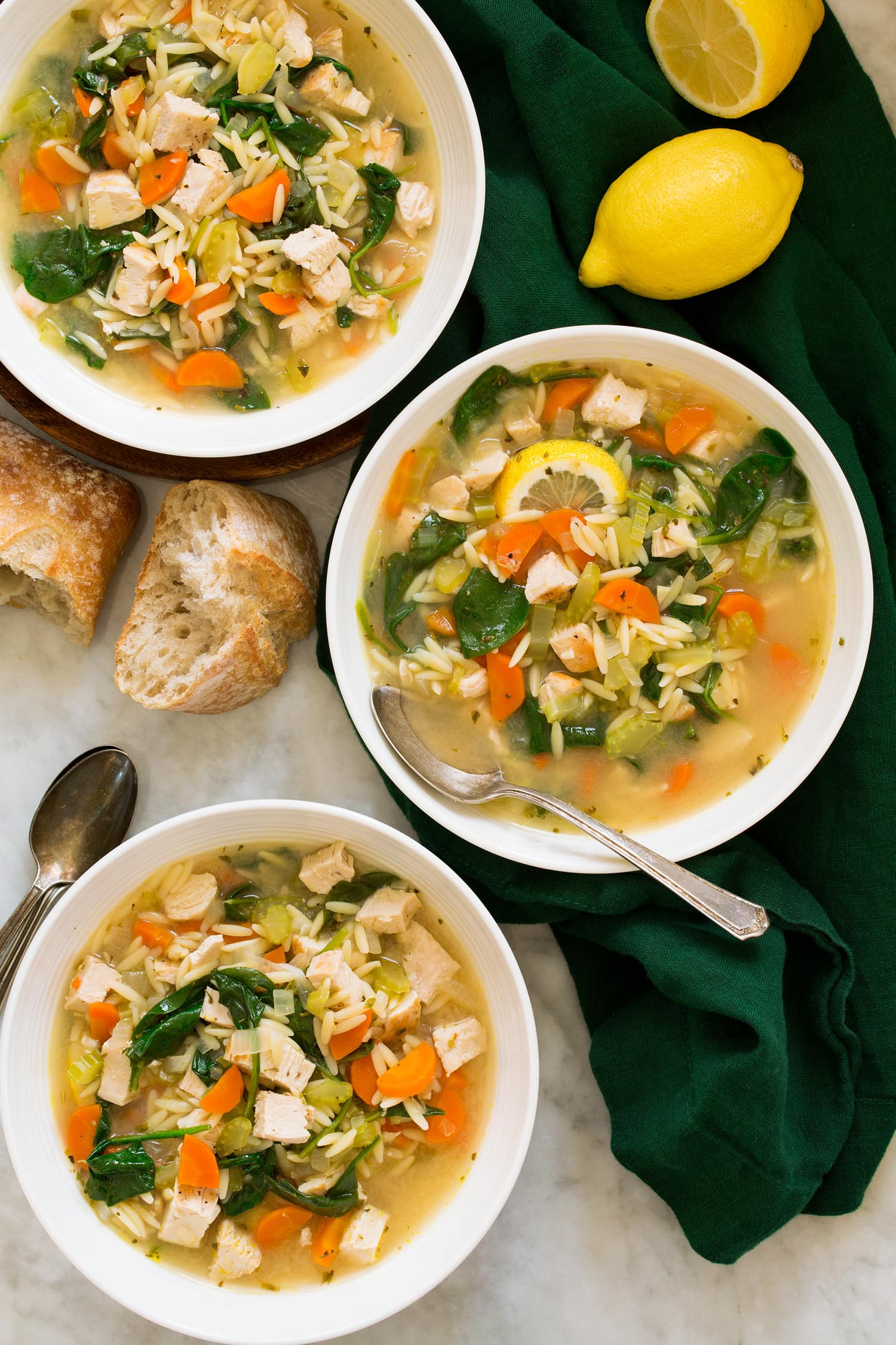 Three bowls of chicken soup with orzo, lemon, spinach, carrots, celery and onions.