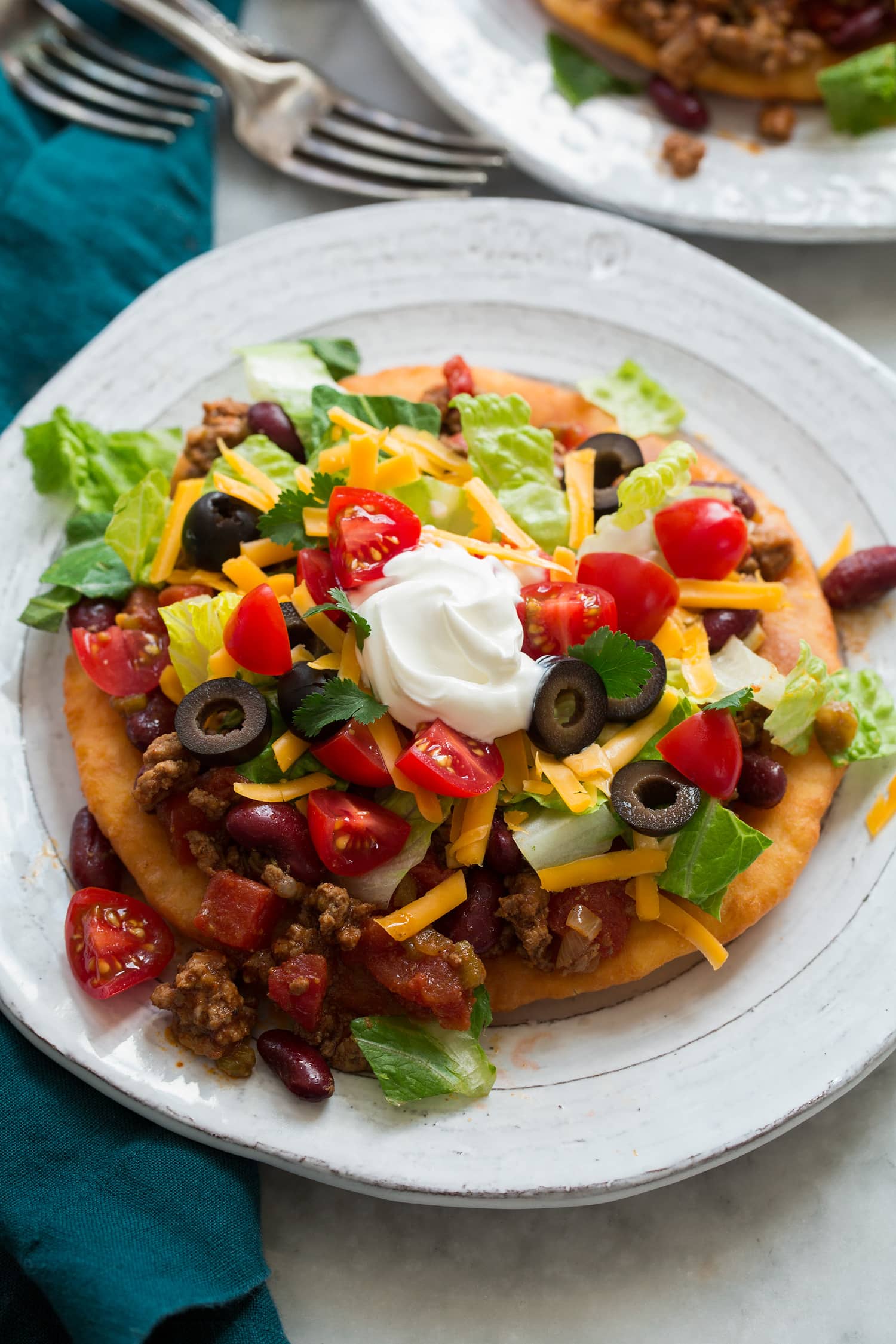 Homemade navajo taco on a plate. Made with homemade fry bread, ground beef and bean filling, lettuce, tomatoes, olives and sour cream.
