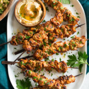 Shish tawook skewers on a platter with parsley and hummus.