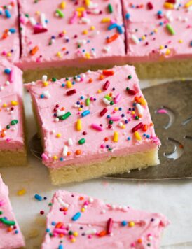 Close up image of sugar cookie bar decorated with pink frosting and sprinkles. It is being scooped up with a serving spatula.
