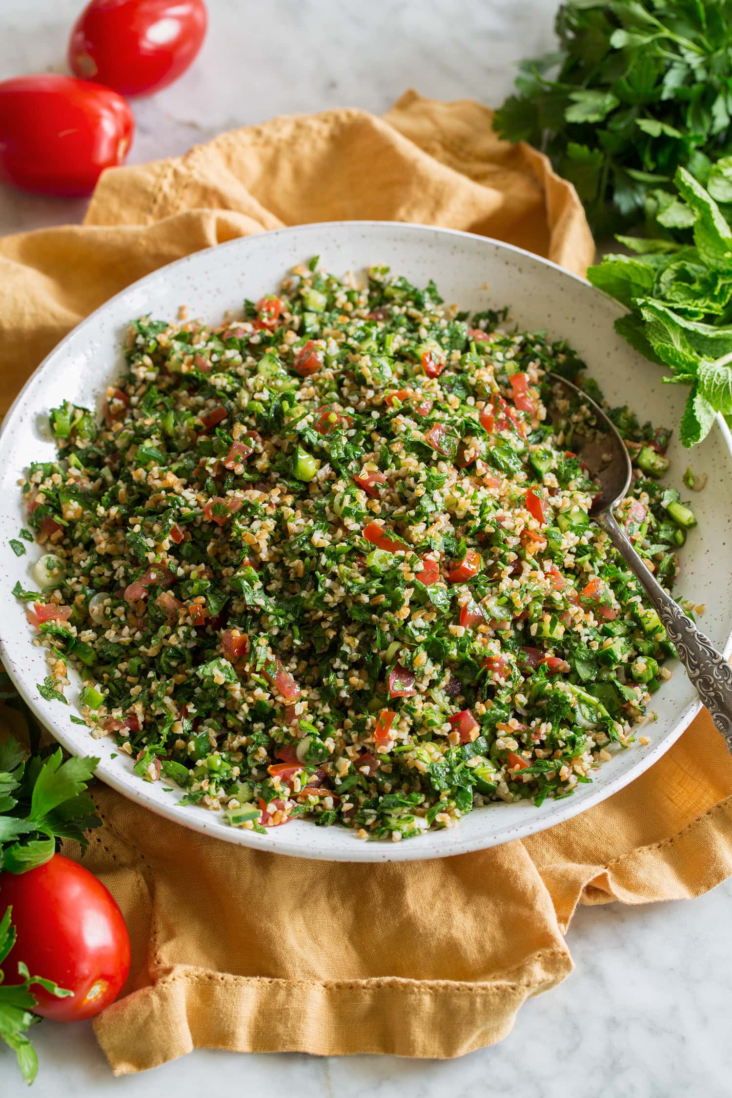 Herb tabbouleh shown in a white ceramic bowl over a yellow cloth.
